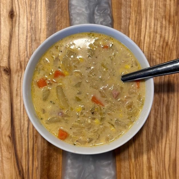 A bowl of ham and vegetable soup sitting on a wooden board.