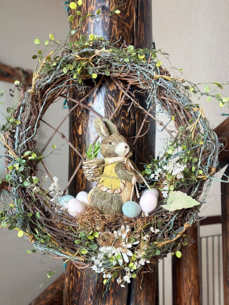 An Easter-themed grapevine wreath decorated with greenery, a sisal bunny, and faux eggs.