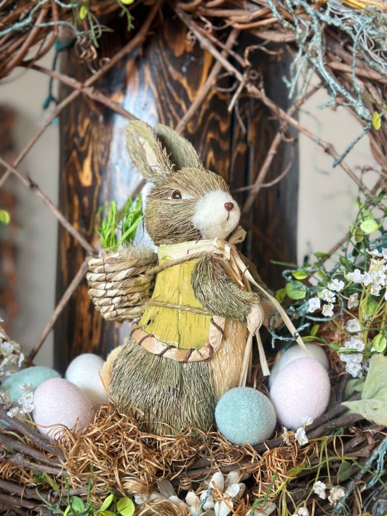 A close up image of an Easter-themed grapevine wreath with a sisal bunny in the middle surrounding by fake Easter eggs.