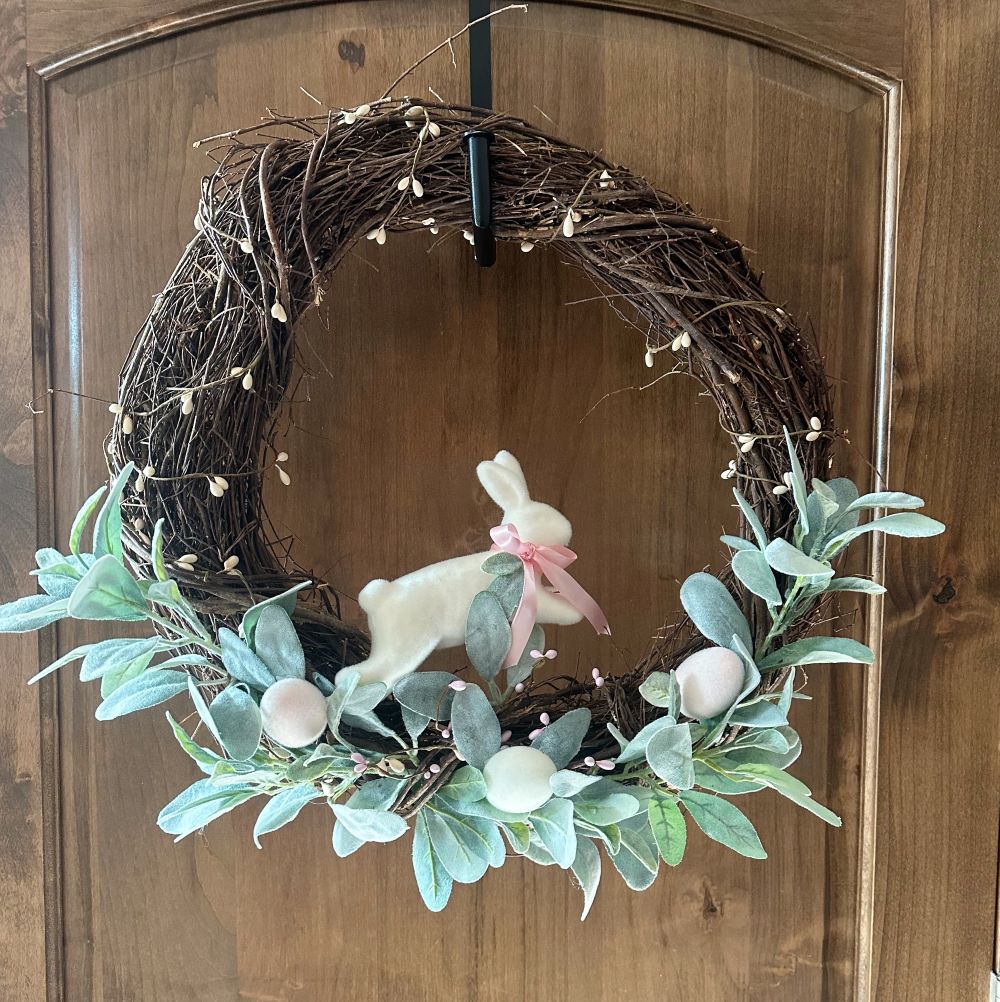 An Easter-themed grapevine wreath decorated with greenery, eggs, and a bunny.