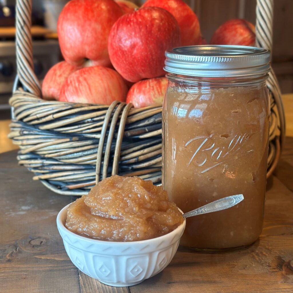 "The Best Homemade Applesauce Recipe" cover image which features a small bowl of the applesauce, a jar of applesauce, and a basket of our homegrown apples.