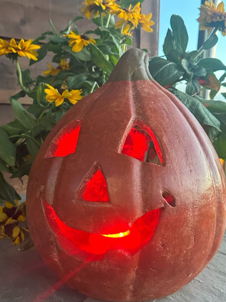 A terra cotta pumpkin outside with a light inside of it.