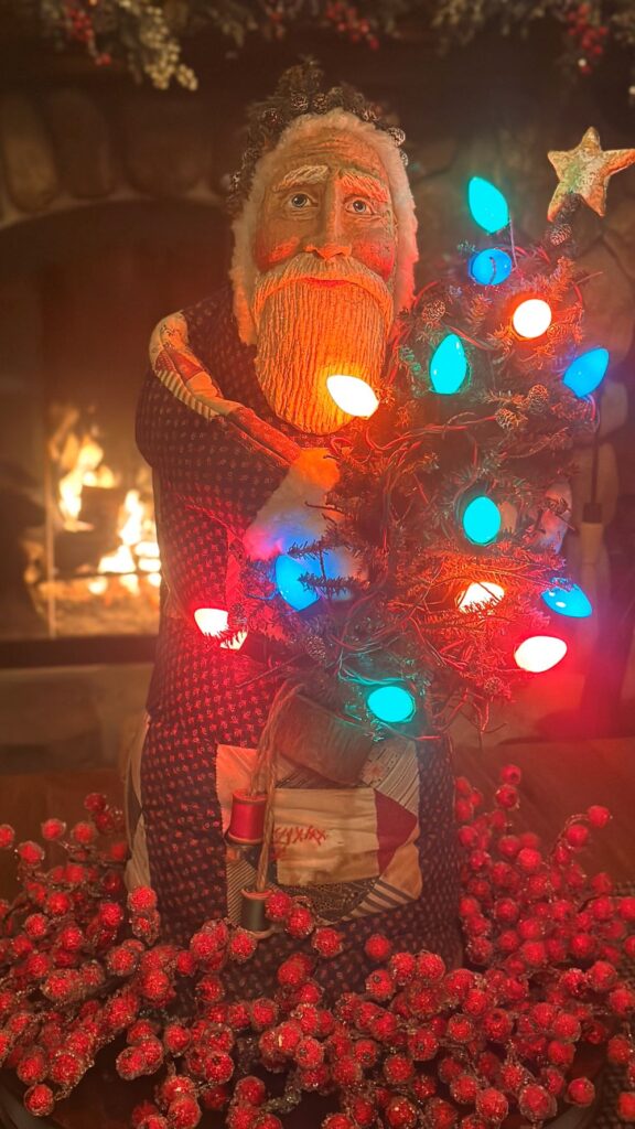 Debra Schoch Tall Quilted Santa Holding Christmas Tree in Front of Fireplace