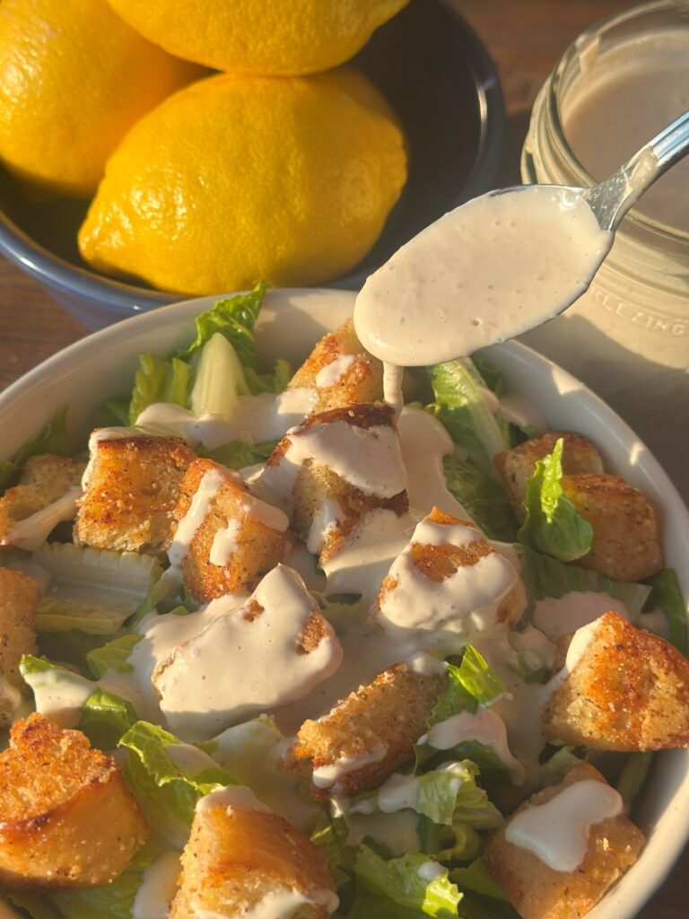 Caesar Dressing Being Drizzled Over a Fresh Salad With Homemade Croutons