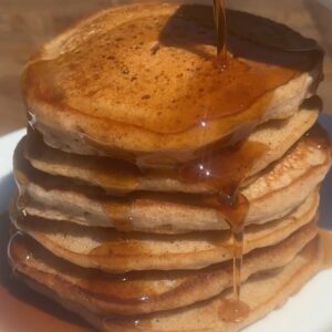 Chai Spiced Pancakes Recipe Cover-- A close up of syrup being poured over a tall stack of yummy chai pancakes on a white plate.