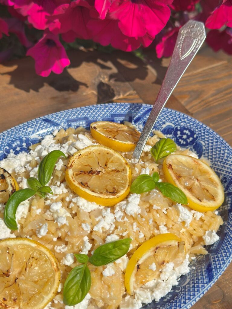 Creamy Lemon Orzo With Feta in a Blue Willow Bowl In Front of Flowers