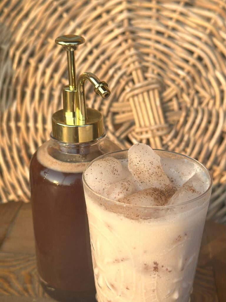 A close up of chai syrup in a bottle next to a chai latte.